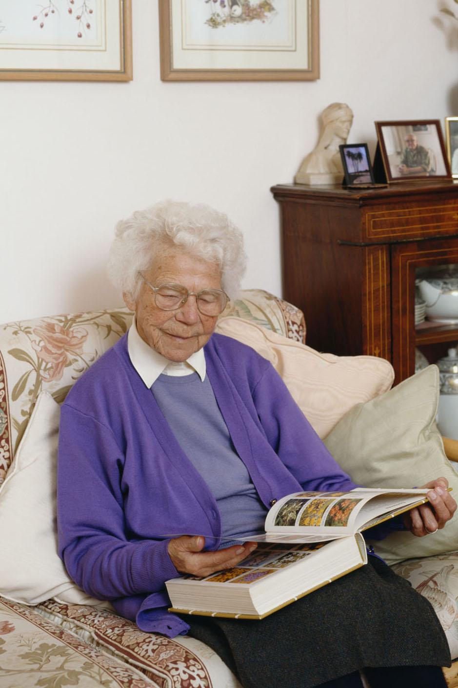 Picture of elderly lady sitting on a settee looking through a gardening book